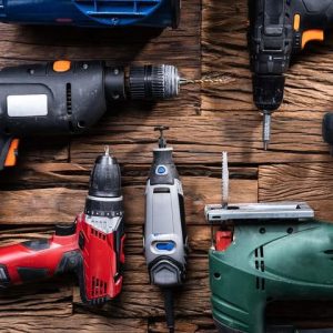 مجموعة أدوات كهربائية صناعية متنوعة على خلفية خشبية، تشمل مثقاباً، منشاراً، ومعدات ورش.